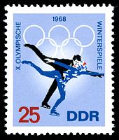 Un timbre avec un fond bleu et deux patineurs de patinage, la date 1968 est centrée sur le haut du timbre avec les anneaux olympiques. Le mot « Winterspiele » est écrit sur le côté droit, les mots « X Olympische » sont écrites sur le côté gauche. Le nombre 25 est dans le coin inférieur gauche et les lettres « DDR » sont dans le coin inférieur droit.