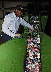 Dans une sorte de trémie-canal métallique peinte en vert, passent des dizaines de canettes de boisson usagées qu’un homme noir de peau, ganté et en uniforme de travail, surveille attentivement.