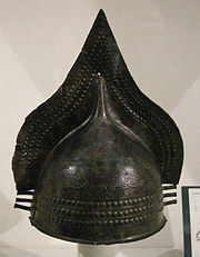 Dans un musée, casque en bronze pointu sur le dessus.