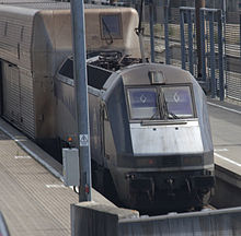 La photographie montre une navette Eurotunnel de face. Le gabarit de la première voiture dépasse largement celui de la locomotive en largeur et en hauteur.