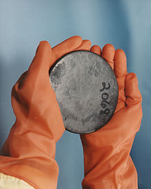 Photographie d'un lingot d'uranium cylindrique tenu dans les mains d'un agent du centre de production.