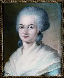 Portrait d'une femme, montrant sa tête, avec une perruque grise. Deux grandes boucles reposent sur la base de son cou. Ses épaules sont couvertes d'un châle léger, de couleur crème.