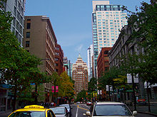 Ground-level view of a street surrounded by numerous high-rise buildings. Along the sides of the road are small trees.