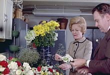 Pat Nixon composant un bouquet de fleurs, assistée d'un homme.