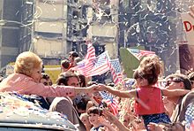 Pat Nixon tend la main à une petite fille de sa voiture, au milieu d'une foule, de drapeaux et de cotillons.