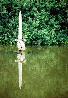 La photographie montre la statue d'une épée dans une main émergeant d'un lac.