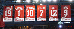 Photo couleur des 6 bannières rouges des maillots retirés des Red Wings de Détroit. De gauche à droite : Yzerman 19, Sawchuk 1, Delvecchio 10, Lindsay 7, Abel 12, Howe 9.