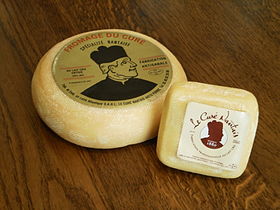 La photographie couleur représente deux fromages, un petit, carré, et un moyen, circulaire. Les deux portent une étiquette avec une tête de curé et la mention Modèle:Curé nantais.