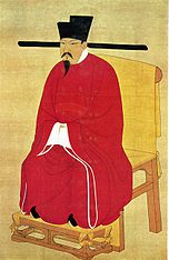 Peinture d'un homme assis sur une chaise en bois, vêtu d'une robe en soie rouge, de chaussures noires, d'un chapeau noir et portant une moustache et une barbichette noires