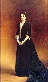 Marie Kann en 1882 : portrait en pied, robe longue foncée, mains gantées jointes.