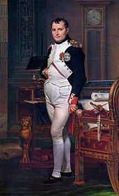  Napoléon debout, une main dans le gilet. Autour de lui, un bureau, un fauteuil, une pendule