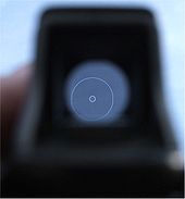 Mire en verre de forme trapézoïdale montée sur un fusil d'assaut FN P90. Ici, le réticule est blanc et en forme de large cercle.