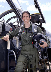 Une femme en uniforme de pilote devant le cockpit ouvert d'un avion de chasse