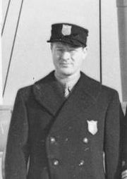 Photographie en noir et blanc montrant un homme vêtu d'une casquette et d'un manteau.