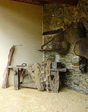 Dans le coin d'une pièce aux murs de pierres, un vieil établi de bois autour duquel sont disposés des filets et des nasses de pêcheur.