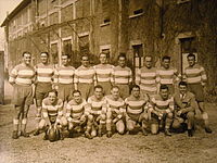 Photo sépia représentant 16 personnes devant un bâtiment en briques datant des années 1930.