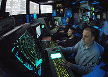 Membres d'équipage en train de surveiller des écrans radars lumineux dans un environnement sombre.