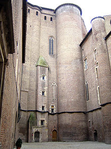 La photographie couleur montre une cour du palais de la Berbie. Les tours et les murailles en brique rouge sont immenses en comparaison avec la porte.