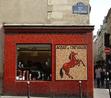 Devanture d'un magasin de briques rouges sur lequel est écrit « achat de chevaux », un cheval étant représenté.