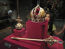 Dans un écrin rouge en vitrine figurent un sceptre richement décoré de joyaux dont le manche est blanc et semble clairement fait d'ivoire, ainsi qu'une couronne d'or décorée elle aussi de joyaux, de perles, et d'autres parties en ivoire.