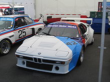  BMW M1 Procar blanche peinte dans sa diagonale aux couleurs de BMW Motorsport exposée dans un stand