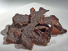 Tas de cinq ou six tranches brun foncé, enchevêtrée, de viande gondolée par le séchage.