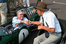 Photo de Jack Brabham (à gauche dans la Brabham BT19) et de Stirling Moss (à droite dans un fauteuil).