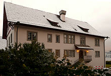 La maison abritant l'Institut C. G. Jung à Küsnacht. Il s'agit d'une petite maison vue de face, le toit recouvert de neige et tout autour de laquelle se trouvent des bosquets de conifères. La façade est légèrement de couleur rosée.