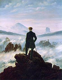  Tableau d'un homme debout tournant le dos au spectateur. Il est en haut d'une montagne, entouré de nugages et de brouillard. Il est vêtu de noir, en vif contraste avec les blancs, les roses et les bleus du ciel. Au lointain, on peut distinguer des affleurements de roches.