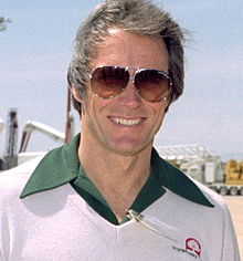 Photographie de Clint Eastwood en 1981. Il porte des lunettes de soleil, a les cheveux grisonnants et porte une chemise surmontée d'un pull