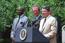 Photographie de Louis Gossett, Clint Eastwood et Ronald Reagan en plein discours, devant un pupitre qui porte un micro