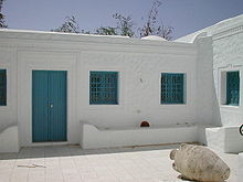 Cour intérieure d’un houch avec ses murs blancs, sa porte et ses grilles aux fenêtres de couleur bleue.