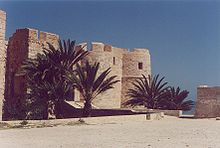 Façade du fort Borj El Kebir de Houmt Souk, partiellement masquée par des palmiers.