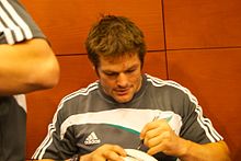 McCaw signe de la main gauche un ballon de rugby à XV présenté par un fan.