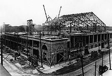 Photo du Forum de Montréal en construction ; il est entouré de matériaux de construction, d'échelles et deux grues sont visibles en arrière plan.