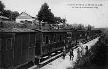 Avant 1914, un train est arrêté en gare avec des habitants sur le quai posant pour le photographe. Le bâtiment voyageurs est visible en haut de la tranchée.