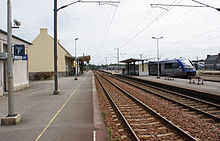 L'intérieur de la gare vu en direction de Rennes. À gauche, les toilettes et le bâtiment voyageurs avec sa marquise ; au centre les voies et le quai central avec son abri. Un X 73500 des TER Bretagne est stationné sur la voie de Lannion.