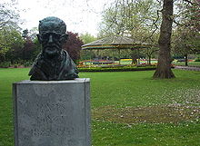 Bronze bust of Joyce in a green park. The bust is poorly lit and only the forehead can be made out clearly. The bust is atop a pedestal saying "JAMES JOYCE 1882–1941".