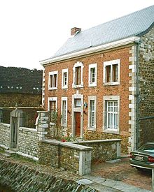  Maison en briques et pierre de taille, toit d’ardoise, à un étage, porte d’entrée centrale, précédée d’un jardinet clos.