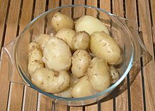 Pommes de terre primeurs de Jersey, bouillies, dans un plat de verre transparent posé sur une table en lattes de bois.