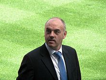 Portrait large de John Wark à Portman Road. L'ancien joueur de Liverpool est habillé d'un costume et d'une cravate bleue.