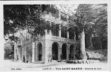 Photo en noir et blanc représentant un cocotier du Chili devant une demeure ancienne (villa Saint Martin) pourvue d'arcades au rez-de-chaussée et de loggias au premier étage et au deuxième étage.