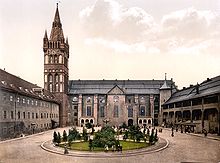 Photographie en couleurs (entre 1890 et 1905) de la cour du château de Kœnigsberg, près duquel était bâtie la maison natale d'Hoffmann. Autour d'un petit jardin circulaire comportant quelques arbres, se dressent les trois bâtis du château et, à gauche, s'élance un clocher de type gothique surmonté d'une horloge.
