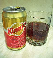 La photo couleur représente une canette de kinnie rouge en bas et or en haut. À droite, un verre présente la boisson : de couleur ambre sombre et montrant la présence de bulles, il a l'aspect d'une boisson au cola.