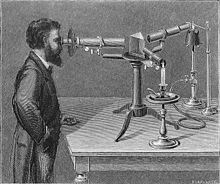 Image ancienne représentant un homme barbu devant un spectroscope ancien dont on voit le prisme et la bougie.