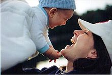 Femme tenant un bébé au dessus de son visage. La femme et l'enfant arborent un grand sourire