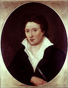  Portrait en buste, d'un homme portant une veste noire et une chemise blanche de travers et ouverte sur sa poitrine.