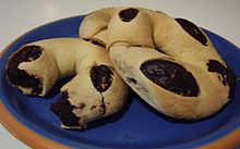 La photographie montre trois gimblettes. Leur pâte gonflée laisse apercevoir, par ses ouvertures, la garniture cacaotée. Une des pâtisseries est coupée afin de montrer sa section.