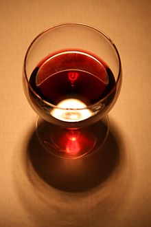L'illustration en couleur montre un verre de vin prise par dessus. Le vin limpide et brillant est de couleur rouge rubis nuancé de brun. Le reflet sur la table donne une couleur rose très brillante