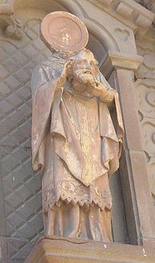 Statue en pied de saint Hilarian, tenant sa tête dans ses mains, au devant d’une niche.
